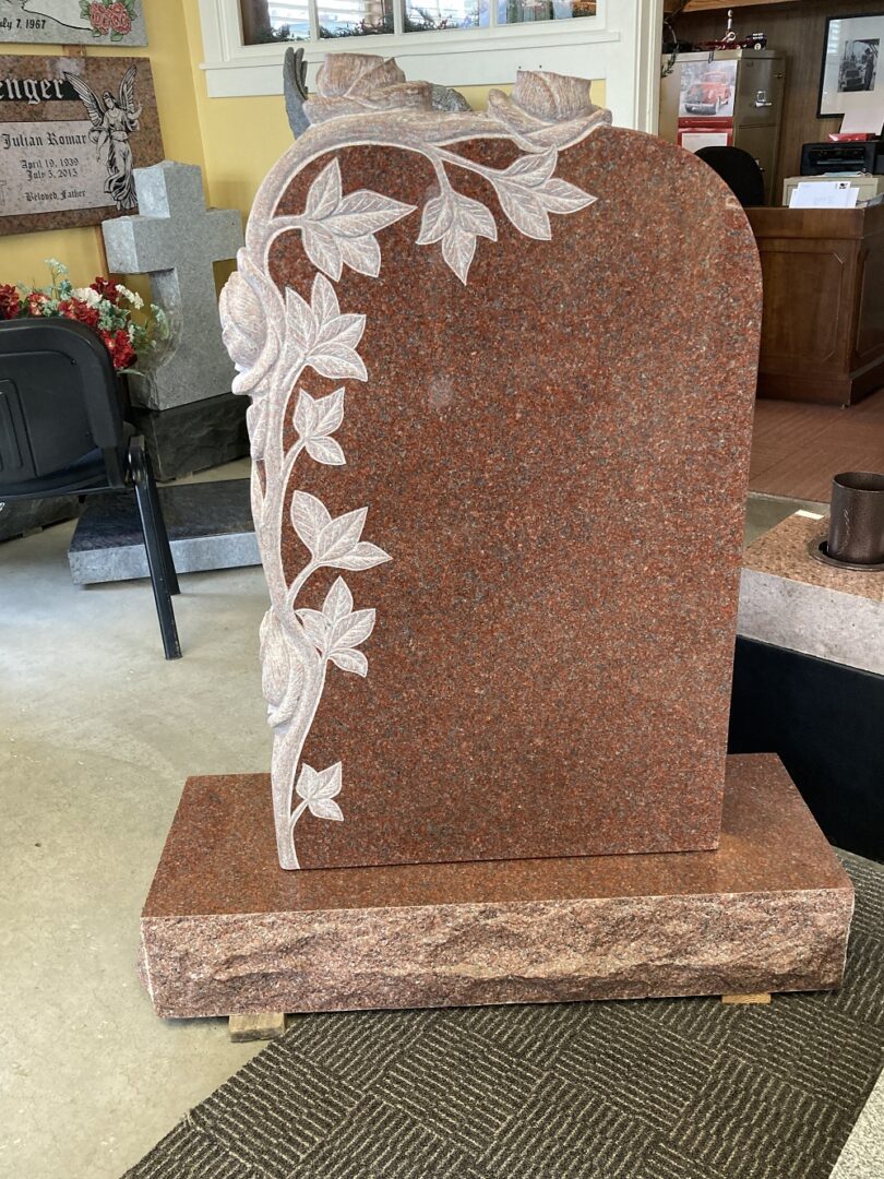 A red granite tombstone with branches and leaves